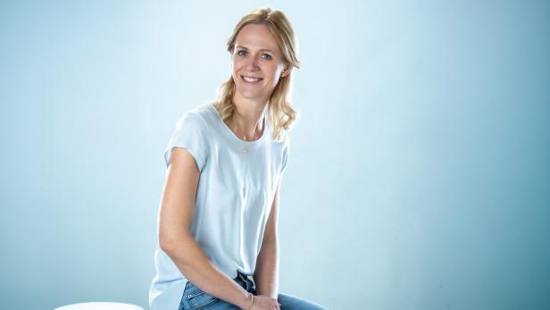 Porträt einer lächelnden Frau vor hellblauem Hintergrund.