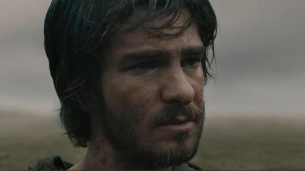 Andrew Garfield blickt mit ernstem, schmutzigem Gesichtsausdruck in einer trüben, weiten Landschaft in die Ferne.