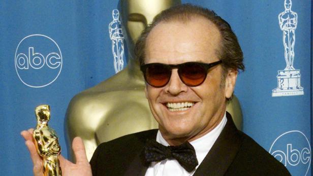 Jack Nicholson lächelt mit Sonnenbrille und Smoking vor einem blauen ABC-Hintergrund und hält eine goldene Oscar-Trophäe in der Hand.