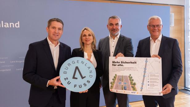 Vier Anzugträger und eine Frau präsentieren ein „Burgenland zu Fuß“-Schild und ein Plakat zur Verkehrssicherheit.