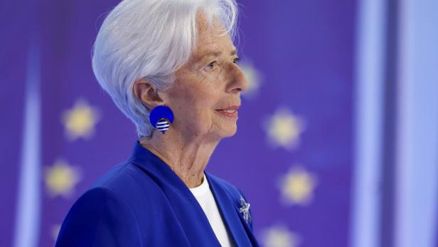 Christine Lagarde trägt ein blaues Kostüm vor einem violetten Hintergrund mit angedeuteten gelben Sternen.