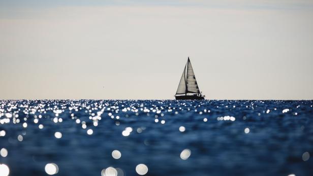 Segelboot auf glitzerndem Meer unter hellem Himmel.