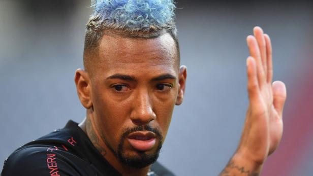 Jérôme Boateng mit blau gefärbten, lockigen Haaren trägt ein schwarzes Trikot des FC Bayern München und hebt die Hand.