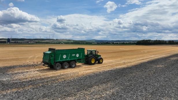 Traktor mit grünem Anhänger fährt über ein abgeerntetes Feld unter wolkigem Himmel.