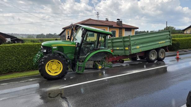 Grüner John-Deere-Traktor mit Anhänger steht auf nasser Straße vor einem Haus.