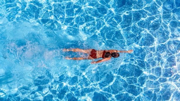 Eine Person in roter Badekleidung schwimmt in einem hellblauen Pool.