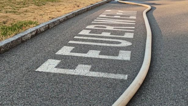 Ein Feuerwehrschlauch liegt auf einer Straße mit dem Schriftzug „FEUERWEHR“.