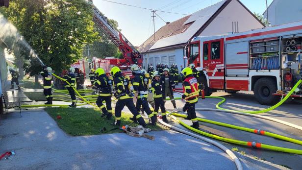 Feuerwehrleute bekämpfen einen Brand mit Schlauchleitungen und Drehleiter vor einem Haus.
