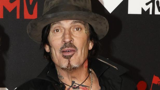 Tommy Lee trägt einen Hut und ein schwarzes Hemd vor einer MTV-Hintergrundwand.