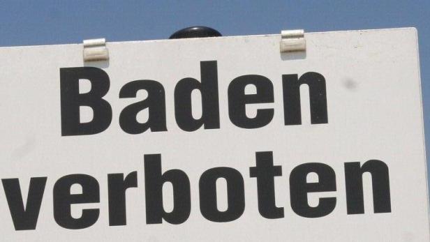 Schild mit der Aufschrift „Baden verboten“ an einem Seeufer.