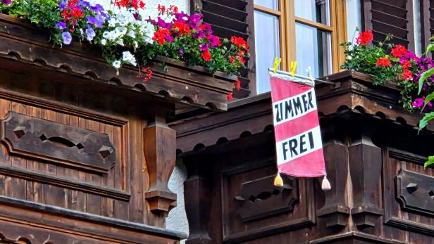 Holzfassade mit bunten Blumenkästen und einem hängenden ZIMMERT FREI-Schild.