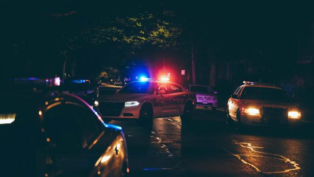 Polizeiautos mit Blaulicht blockieren eine dunkle, nasse Straße bei einem Einsatz.