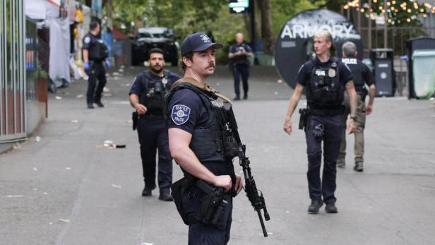 Mehrere bewaffnete Polizisten stehen auf einer Straße, einer im Vordergrund mit Gewehr und SEATTLE POLICE-Aufnäher.