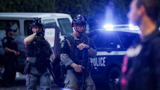 Bewaffnete Beamte des Seattle Police SWAT-Teams stehen vor einem Polizeiwagen mit eingeschaltetem Blaulicht.