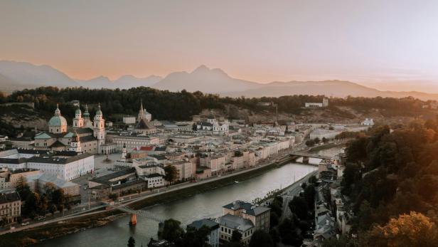 Blick über Salzburg mit Fluss, Altstadt und Bergen im Abendlicht.