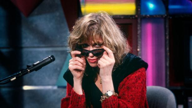 Carly Simon sitzt am Klavier und zieht ihre Sonnenbrille zurecht.