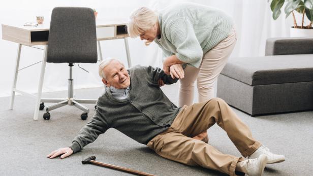 Das Bild zeigt einen alten Mann, der gestürzt ist. Seine Frau ist gerade dabei, ihm aufzuhelfen.
