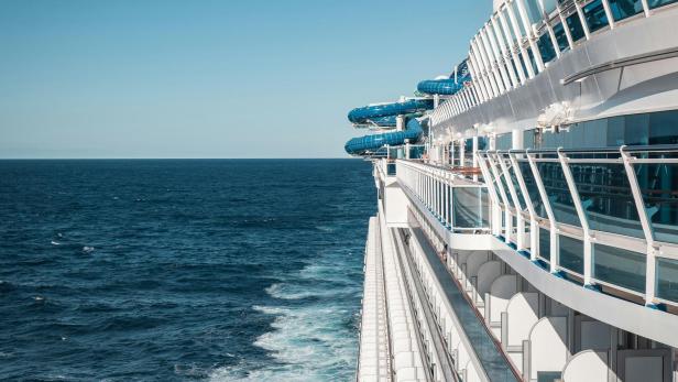 Kreuzfahrtschiff auf offener See mit Decks und blauen Wasserrutschen.