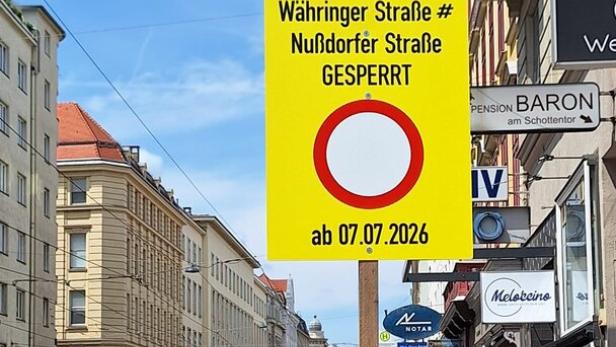 Gelbes Straßenschild kündigt die Sperrung der Währinger und Nußdorfer Straße ab 07.07.2026 an, an einer Wiener Straße mit Autos und Fußgängern.