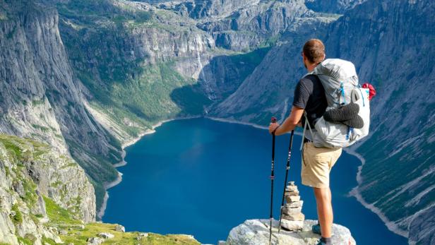 Wanderer mit Rucksack und Trekkingstöcken blickt über ein Bergtal mit See.