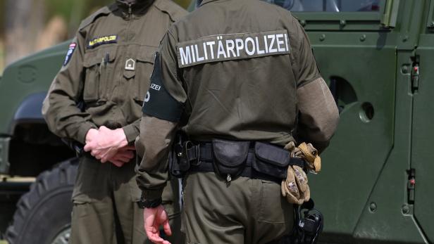 Zwei Militärpolizisten in Uniform stehen vor einem grünen Militärfahrzeug.