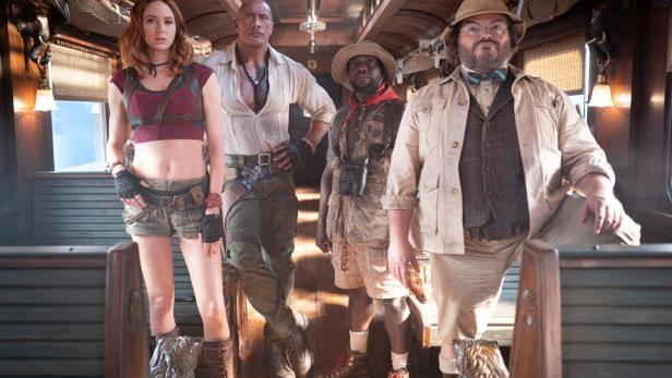 Karen Gillan, Dwayne Johnson, Kevin Hart und Jack Black stehen in Abenteurerkleidung in einem historischen Zugwaggon.