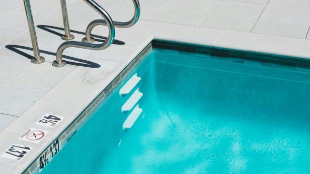 Ein leerer Swimmingpool mit Leiter und türkisfarbenem Wasser.