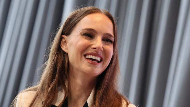 Natalie Portman lächelt fröhlich vor einem grauen Vorhang.
