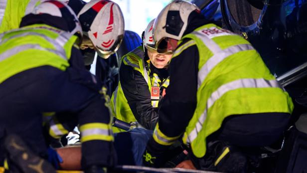 Rettungskräfte in Helmen und Warnwesten arbeiten dicht gedrängt an einer eingeklemmten Person.