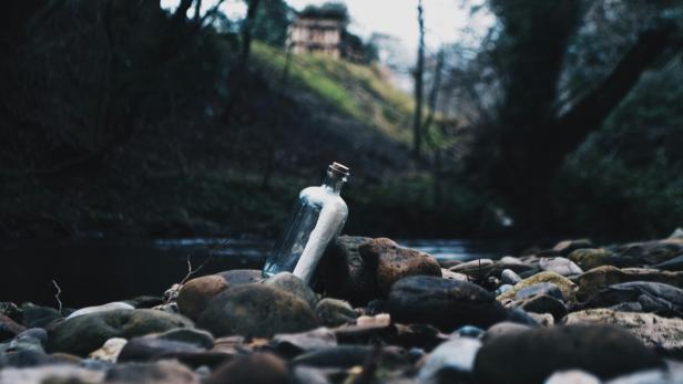 Flaschenpost in einer Glasflasche am Ufer zwischen Steinen.