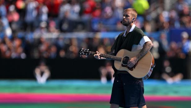Justin Bieber spielt vor einem großen Publikum auf einer bunten Bühne eine Akustikgitarre.