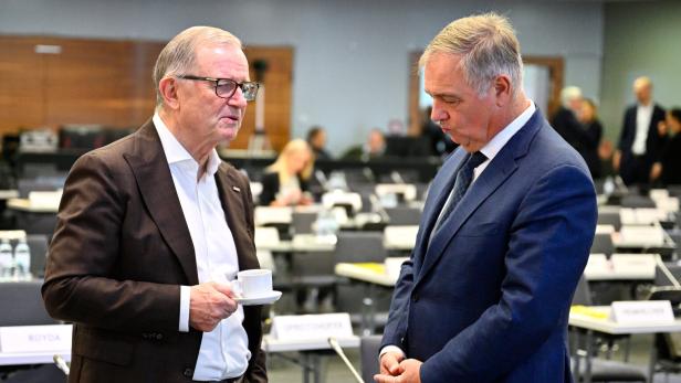 Zwei Männer im Anzug sprechen in einem Konferenzsaal, einer hält eine Kaffeetasse.
