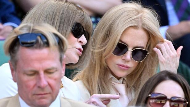 Anna Wintour und Nicole Kidman sitzen nebeneinander auf der Tribüne und tragen beide eine Sonnenbrille.