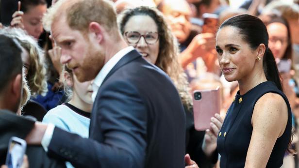 Prinz Harry und Meghan Markle inmitten einer Menschenmenge, die sie mit Smartphones fotografiert.