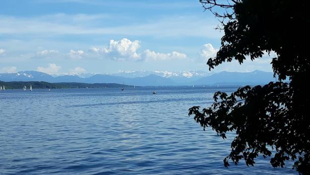 Blick über den Bodensee mit Segelbooten und Bergen im Hintergrund.