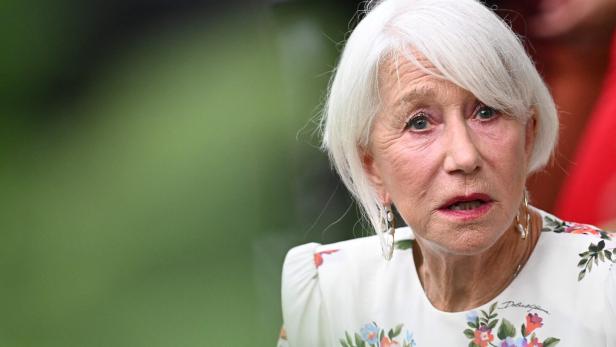 Helen Mirren mit weißem Haar und einem floralen Kleid blickt aufmerksam zur Seite.