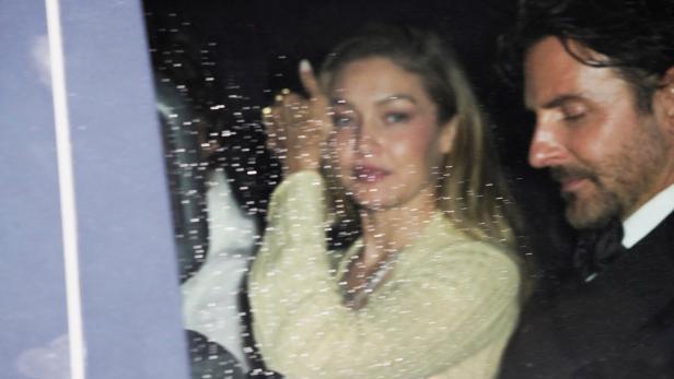 Gigi Hadid und Bradley Cooper sitzen bei Nacht in einem Auto, wobei die Scheibe mit Regentropfen bedeckt ist.