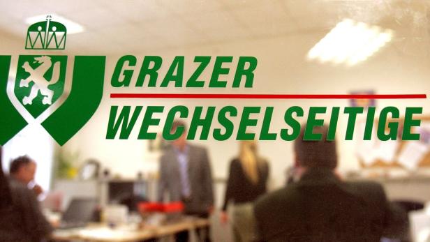 Das Logo der Grazer Wechselseitige Versicherung vor einem Büro mit Mitarbeitern.
