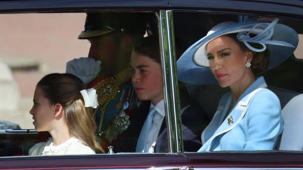Prinzessin Catherine, Prinz George und Prinzessin Charlotte sitzen in einer Kutsche oder einem Auto, begleitet von einem uniformierten Offizier.