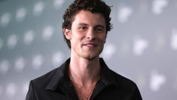 Shawn Mendes lächelt vor einem grauen Hintergrund in die Kamera.