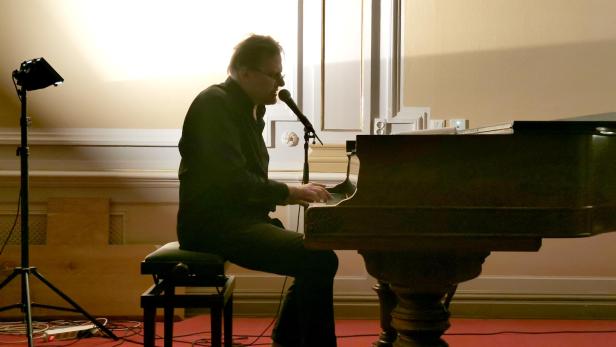 Mann sitzt an Klavier und singt in Mikrofon.