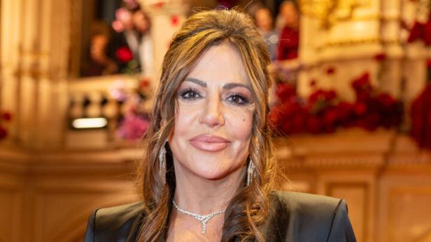 Simone Thomalla in schwarzem Anzug mit Schmuck steht in einem prunkvollen Saal.