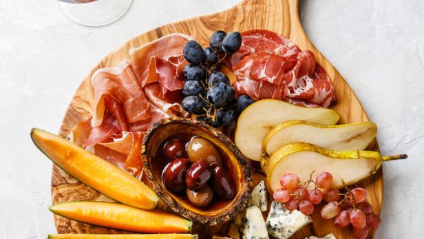 Ein Holzbrett mit Schinken und Käse garniert mit Melone und Birne