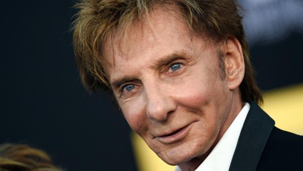 Nahaufnahme des Sängers Barry Manilow mit seinem charakteristischen blonden Haar vor einem dunklen Hintergrund.