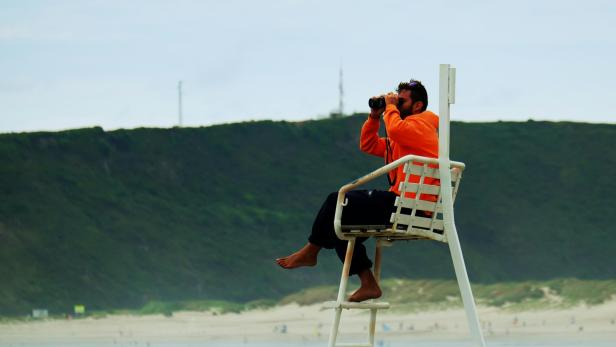 Bademeister auf einem Turm beobachtet den Strand mit dem Fernglas.
