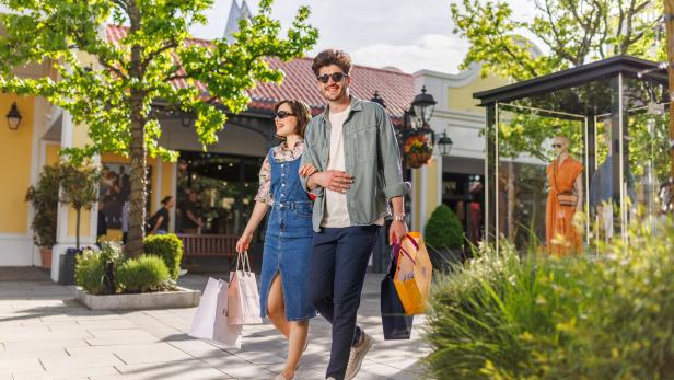 Ein Paar läuft Arm in Arm durch ein Shoppingcenter, mit Einkaufstaschen in der Hand. 
