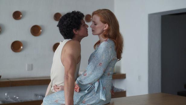 Ein Mann und eine Frau sitzen sich auf einer Küchenarbeitsplatte gegenüber und berühren sich beinahe beim intimen Annähern.