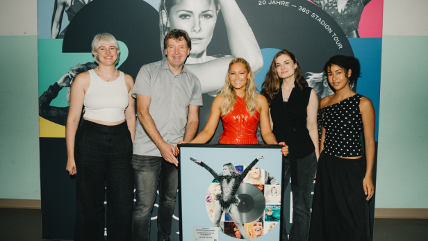 Fünf Personen stehen vor einer Wand mit Helene Fischer-Foto