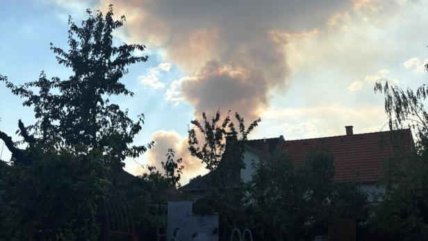 Große, von der Sonne goldgeränderte Wolke über einem Garten mit Pool und Hausdächern.