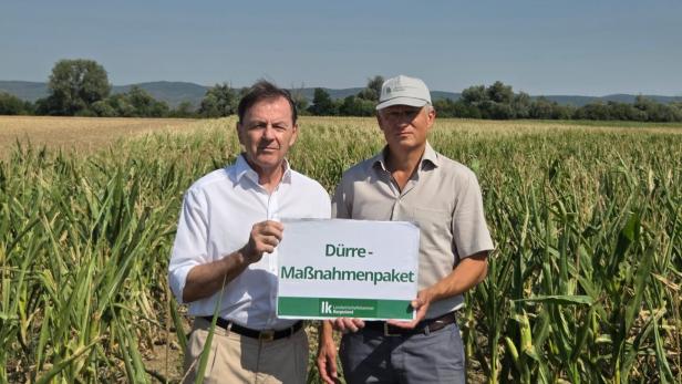 Zwei Männer stehen im Maisfeld und halten ein Schild mit „Dürre-Maßnahmenpaket“.